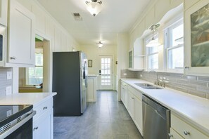 A modern kitchen with white cabinetry, a stainless steel refrigerator, a dishwasher, and a window with a view. - BEE Inn BRENHAM Holiday Cottage - Premium location walking distance to downtown. (Brenham)