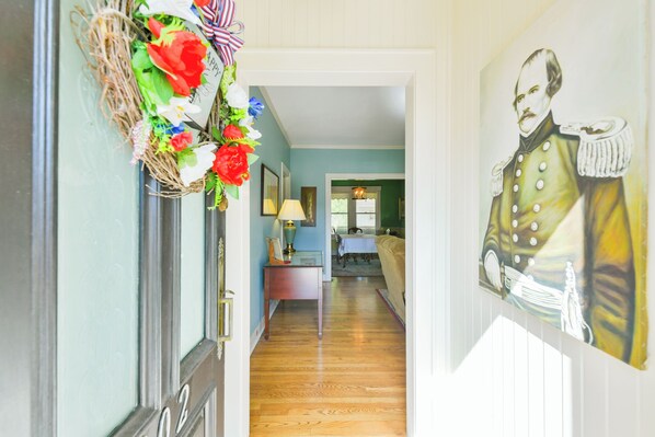 A hallway with a door, a wall-mounted painting, and a dining area in the background. - BEE Inn BRENHAM Holiday Cottage - Premium location walking distance to downtown. (Brenham)