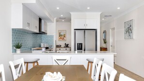 Une cuisine moderne avec des meubles blancs, un réfrigérateur en acier inoxydable et un pare-feu en carreaux bleus.