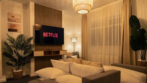 Ein modernes Hotelzimmer mit einem großen Bett, einem an der Wand befestigten Flachbildfernseher, einem Nachttisch, einer Lampe und einer Zimmerpflanze.
