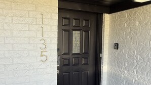 A black door with a decorative glass panel, a white brick wall with the numbers "1135" on it, and a textured white wall on the right.