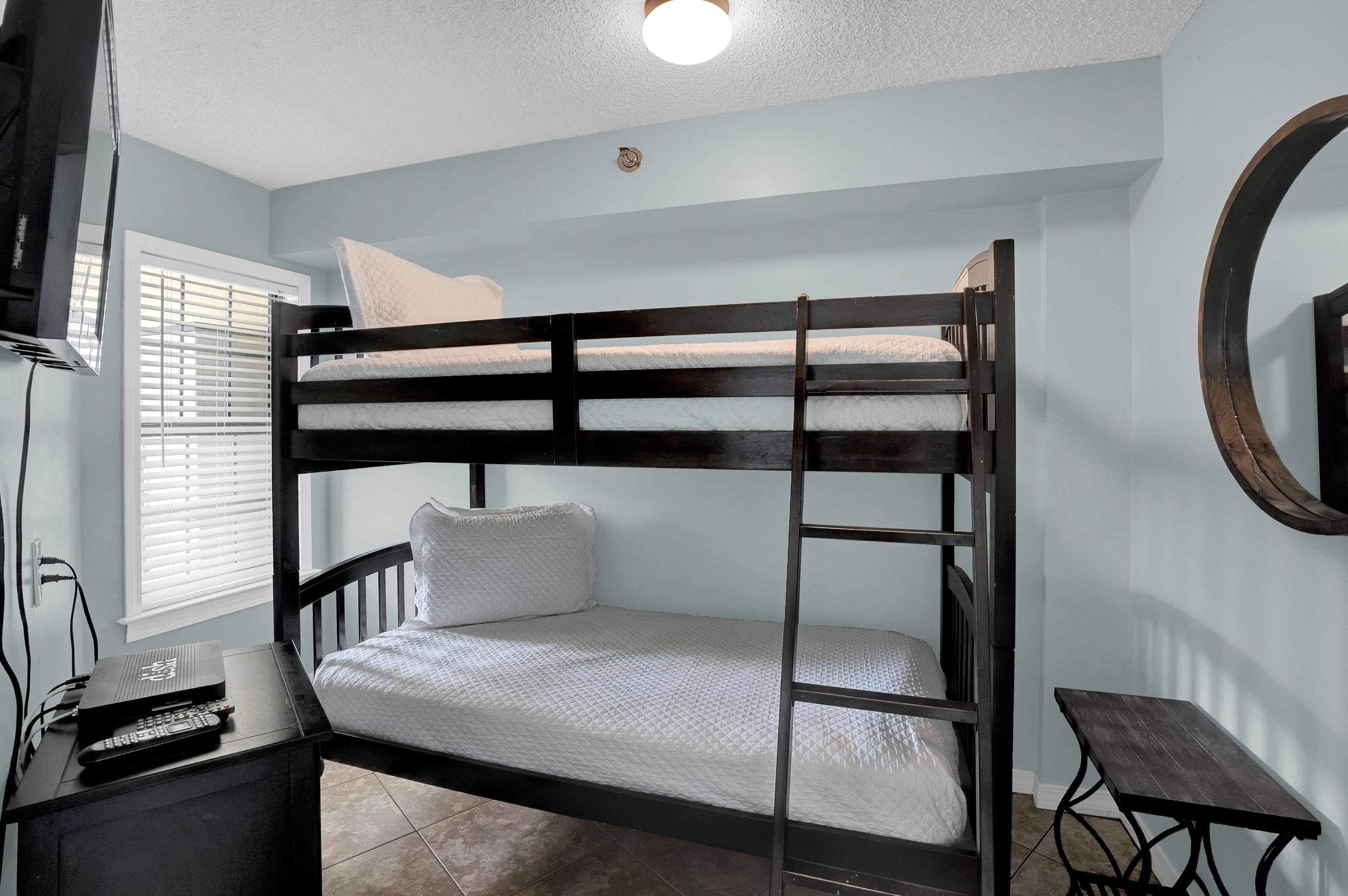 Una cama nido con una escalera, una mesita pequeña y un televisor sobre un mueble.