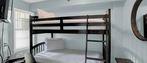 Una cama nido con una escalera, una mesita pequeña y un televisor sobre un mueble.