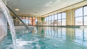 En indendørs swimmingpool med krystalklart vand, et vandfald og store vinduer med udsigt udendørs.