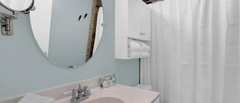 A bathroom with a sink, mirror, towel rack, and a shower curtain.