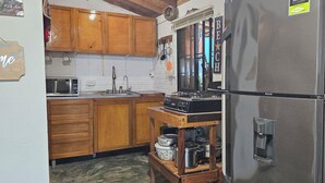 A kitchen with wooden cabinets, a stainless steel refrigerator, a microwave, and a gas stove. - Charming 2-bedroom house with WiFi, AC in Dibulla, ocean view. (Dibulla)