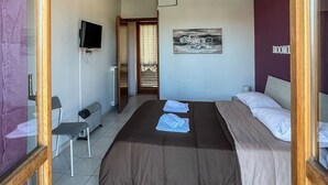 Une chambre dotée d’un grand lit, d’un téléviseur à écran plat fixé au mur, d’un radiateur et d’une porte donnant sur une autre pièce.
