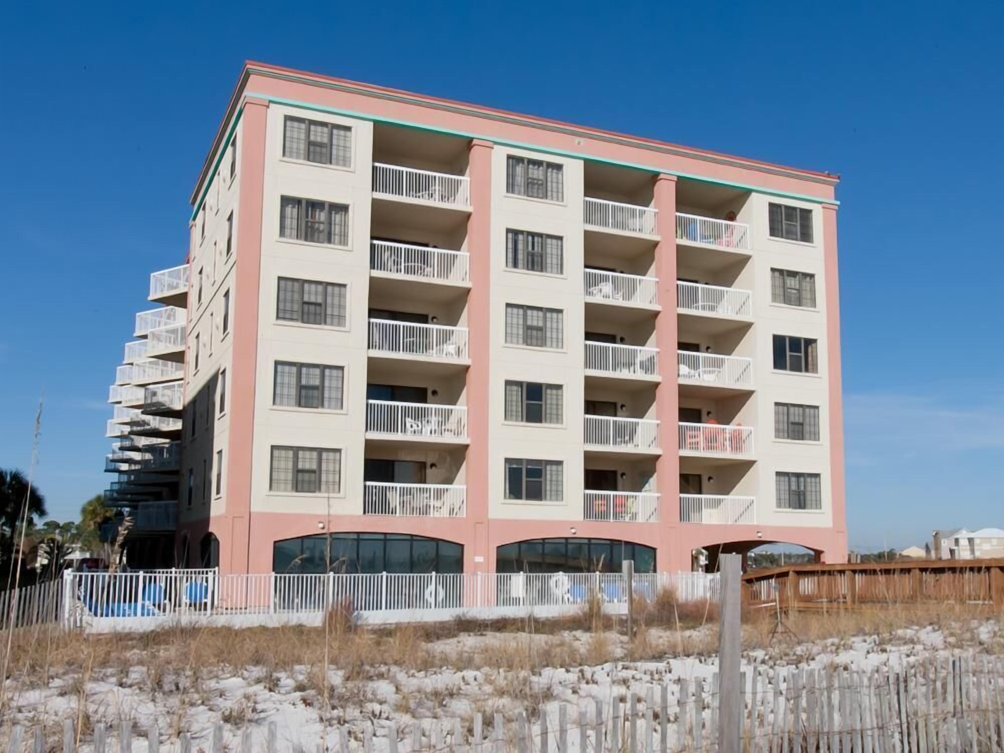 A multi-story hotel with balconies, a flat roof, and a sandy foreground.