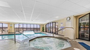 An indoor swimming pool with a hot tub, clear glass walls, and a clock on the wall. - Harbour Place 503 (Orange Beach)