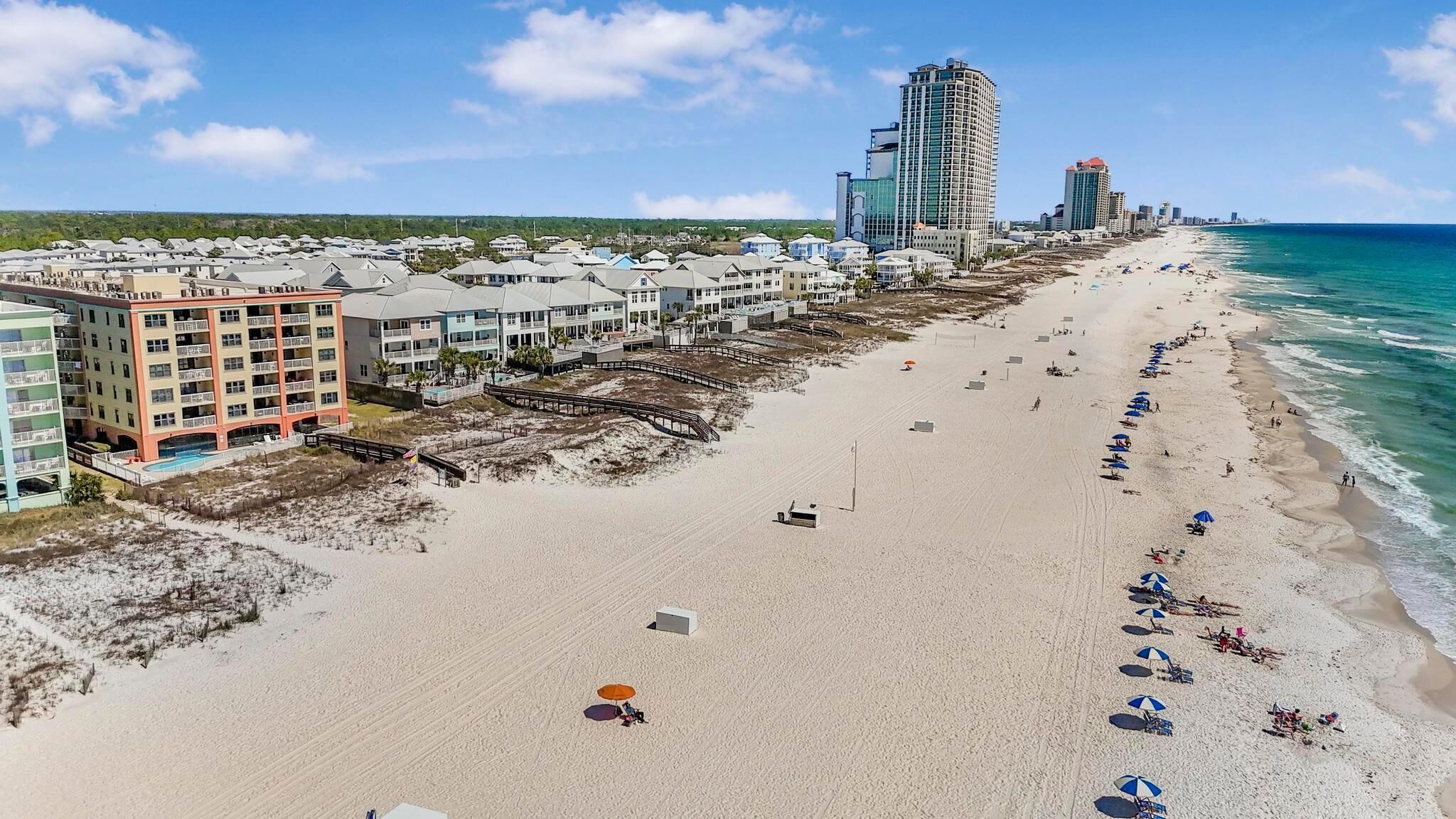A beachside hotel with multiple floors, a boardwalk, and beach umbrellas.