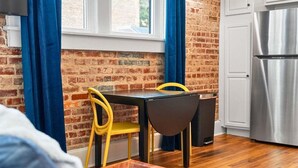 Quarto com parede de tijolos, mesa de jantar com cadeiras, geladeira e janela com cortinas.