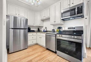 A kitchen with white cabinets, a stainless steel refrigerator, a microwave, and a stove. - Stylish Loft in the Heart of Downtown (Hot Springs)