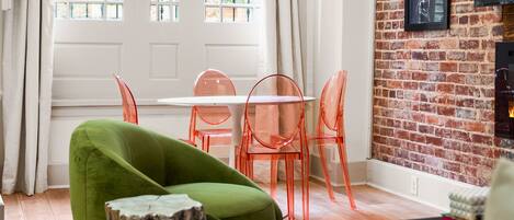 A room with a dining table and chairs, a green armchair, a brick wall, and a fireplace.
