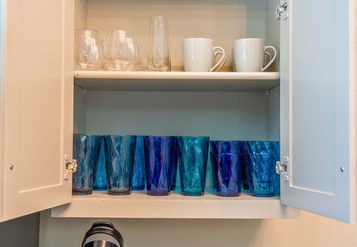 Un mueble con dos estantes; el estante superior contiene cristalería transparente y blanca, y el inferior, cristalería azul.