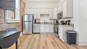 A modern kitchen with white cabinets, stainless steel appliances, and a brick accent wall. - Funky Bungalow Studio · Walk to Bathhouse Row (Hot Springs)