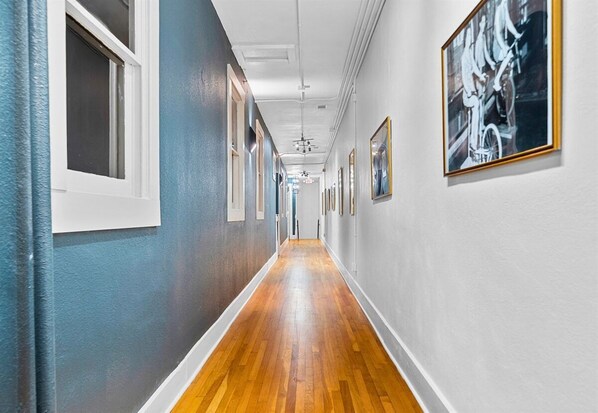 A hallway with wooden flooring, white walls, and framed artwork.