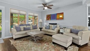 A living room with a sectional sofa, ottoman, coffee table, and a ceiling fan. - 3 BR, Tiled Showers, Hot Tub, King Bed, Smart TV (Fredericksburg)