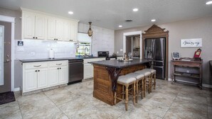 Una cocina amplia con armarios blancos, una isla central con taburetes, un refrigerador y un comedor con mesa y sillas.