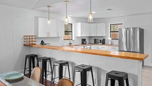 A modern kitchen with white cabinets, a wooden countertop, black stools, and stainless steel appliances. - 6 BR Private Ranch, 2 Hot Tubs, Game Barn (Fredericksburg)