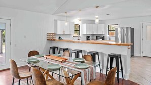 A modern kitchen with white cabinets, stainless steel appliances, and a glass dining table with chairs. - 6 BR Private Ranch, 2 Hot Tubs, Game Barn (Fredericksburg)