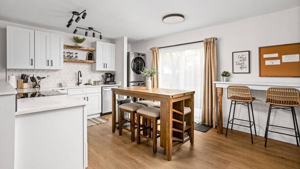 Una cocina moderna con armarios blancos, una mesa de comedor de madera y dos taburetes de bar.
