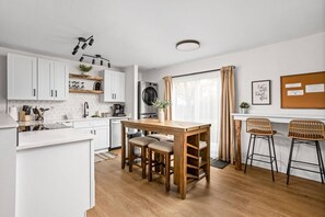 A modern kitchen with white cabinets, a wooden dining table, and two bar stools. - Updated 3BR near Ruoff & Downtown (Noblesville)