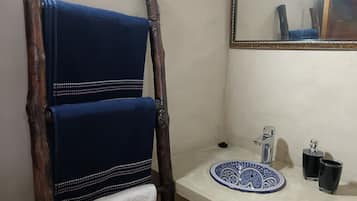 A bathroom with a wooden towel rack holding two towels, a sink with a decorative plate, and two bottles.