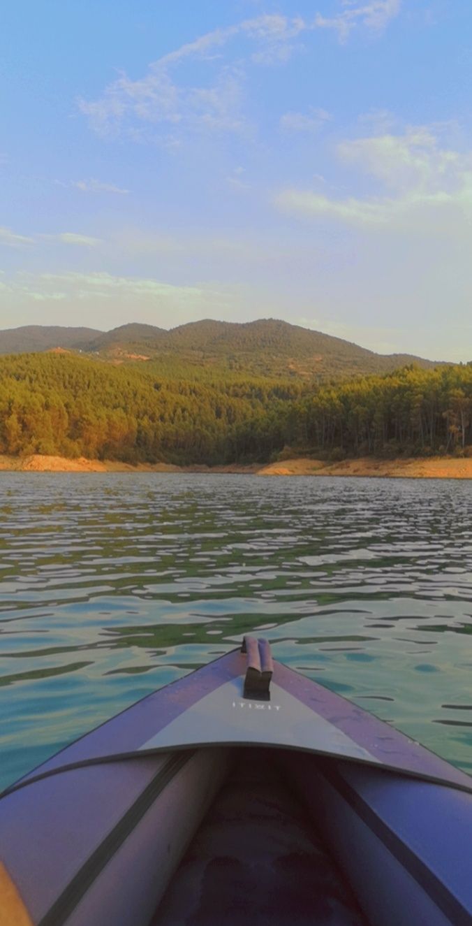 Vue depuis un canoë sur un lac paisible, avec des collines boisées en arrière-plan.