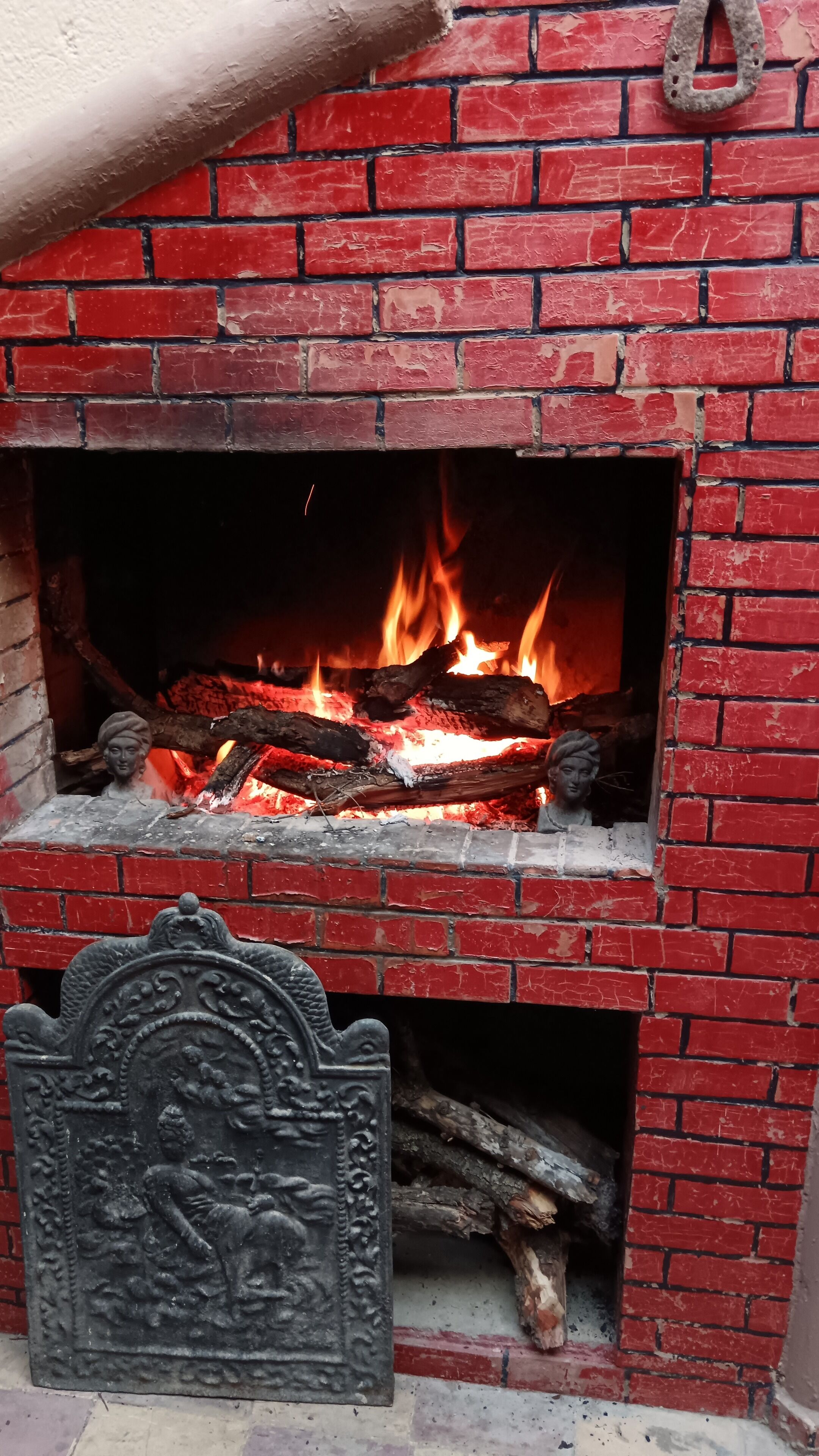 Een rode bakstenen schoorsteenmantel met een decoratief metalen ornament en brandhout.