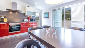 Una cocina moderna con armarios rojos, horno empotrado y un comedor con mesa y sillas.