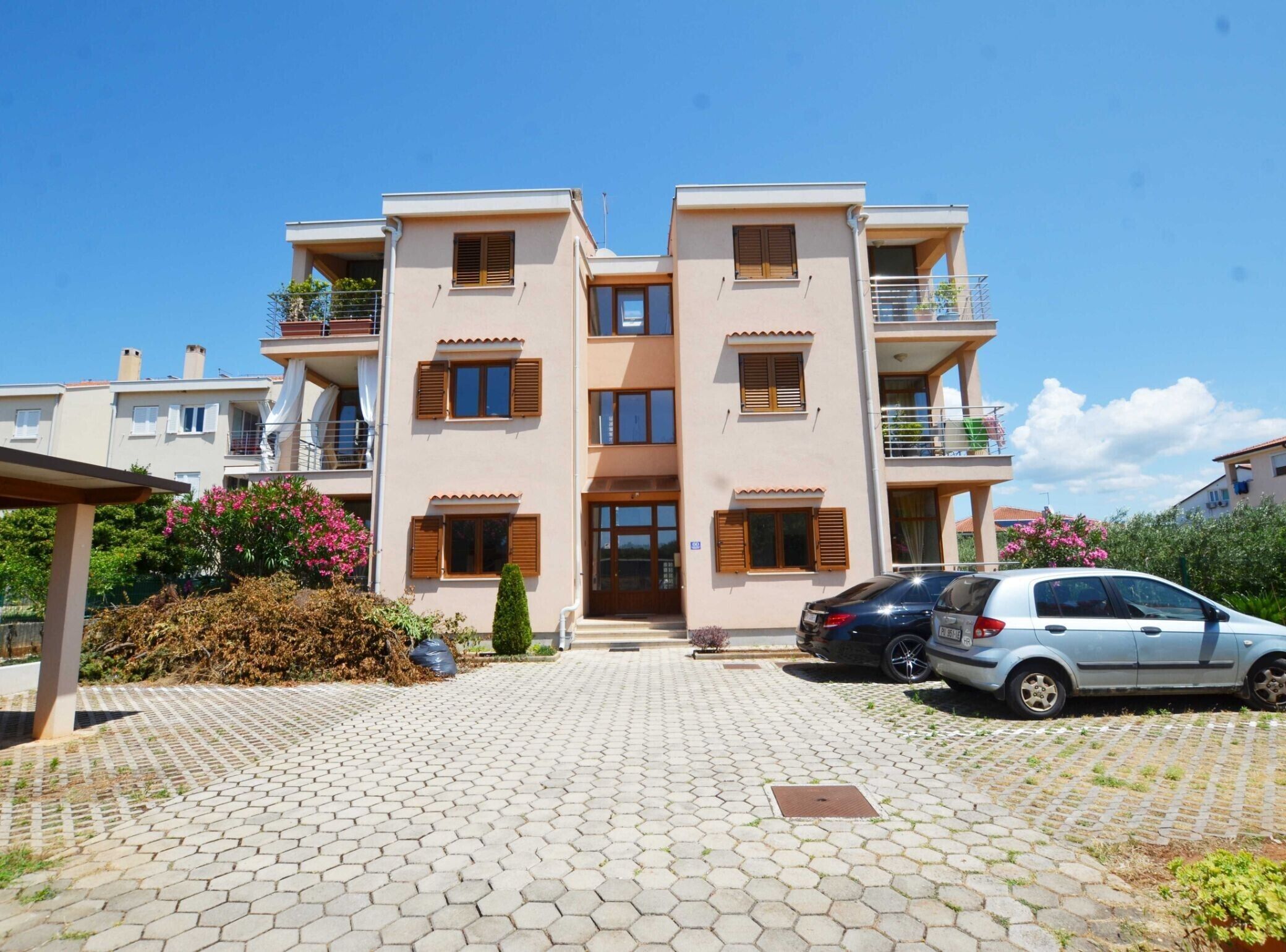 Un immeuble résidentiel à plusieurs étages, doté d’une entrée centrale, de balcons et d’une allée pavée.