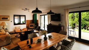Una sala de estar moderna con una mesa de comedor de madera, asientos cómodos, una chimenea y un ventanal con vistas a la vegetación.