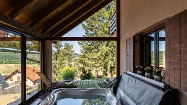 Un jacuzzi en una habitación con ventanas amplias que dan a un jardín y vistas a casas.