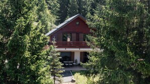 Una cabaña rodeada de un bosque frondoso, con un porche cubierto y zona de estar al aire libre.