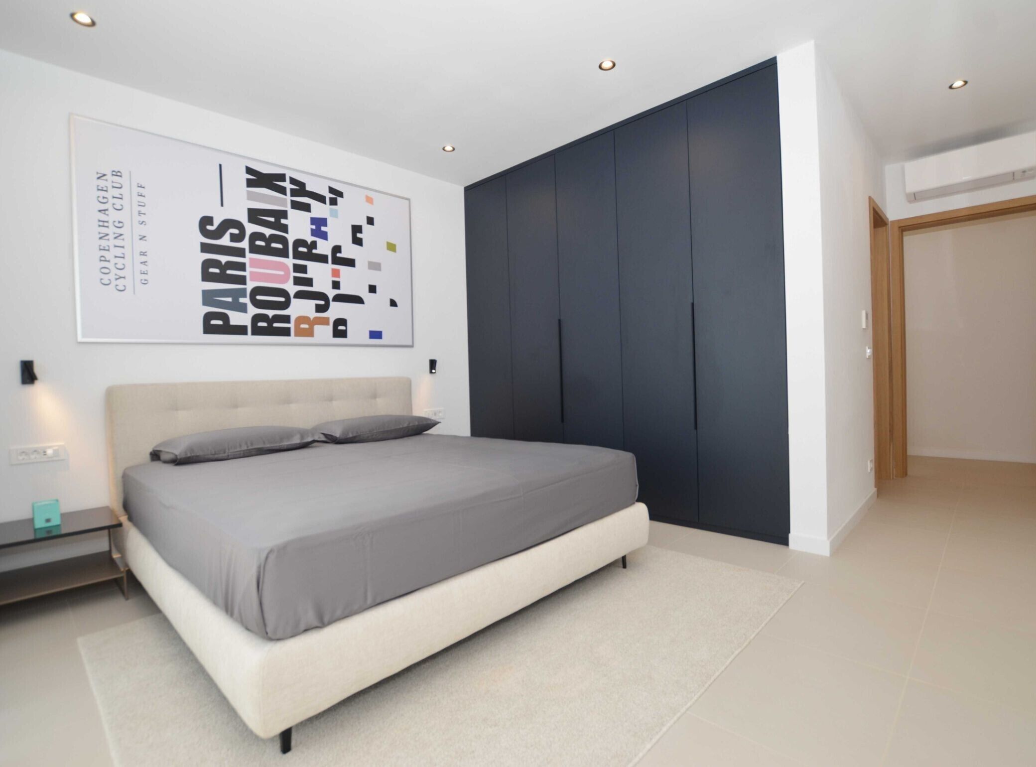 A modern bedroom with a large bed, a dark accent wall, and a poster on the wall.