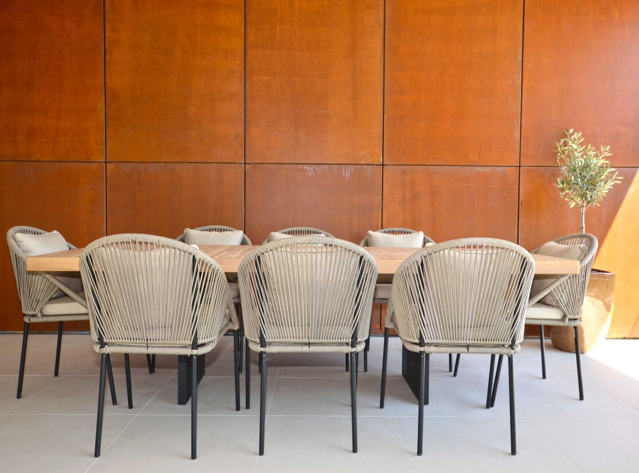 A dining area with a long wooden table and six wicker chairs with black legs.