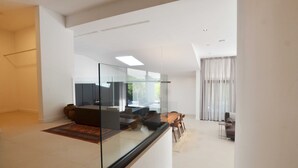 Ein modernes Wohnzimmer mit Glastrennwand, einer Couch, einem Couchtisch und einem Essbereich mit Stühlen.
