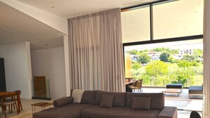 Ein modernes Wohnzimmer mit einer großen Eckcouch, einem Holztisch und Blick auf einen Balkon mit Gartenmöbeln.