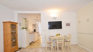 Un espacio habitable compacto con comedor, kitchenette y televisor montado en la pared.