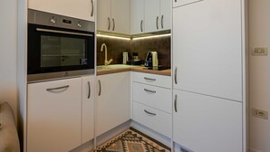 Una cuina compacta amb armaris blancs, forn integrat, rentapesos i cafetera.