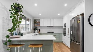 A modern kitchen with a central island, bar stools, a refrigerator, and a hanging plant. - Rye Botanica-Swim Spa, renovated, amazing garden (Rye)