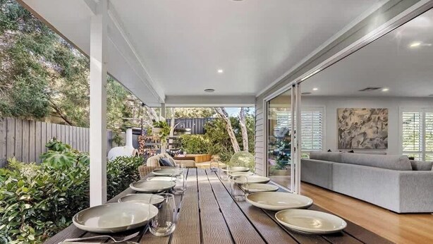 A dining area with a long wooden table set for a meal, a grey sofa, and a view of the garden. - Rye Botanica-Swim Spa, renovated, amazing garden (Rye)