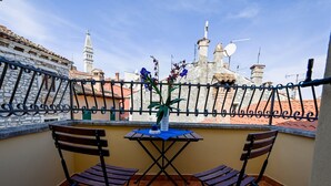 Een balkon met twee stoelen en een tafel, met uitzicht op een stadsgezicht met historische gebouwen en een toren.