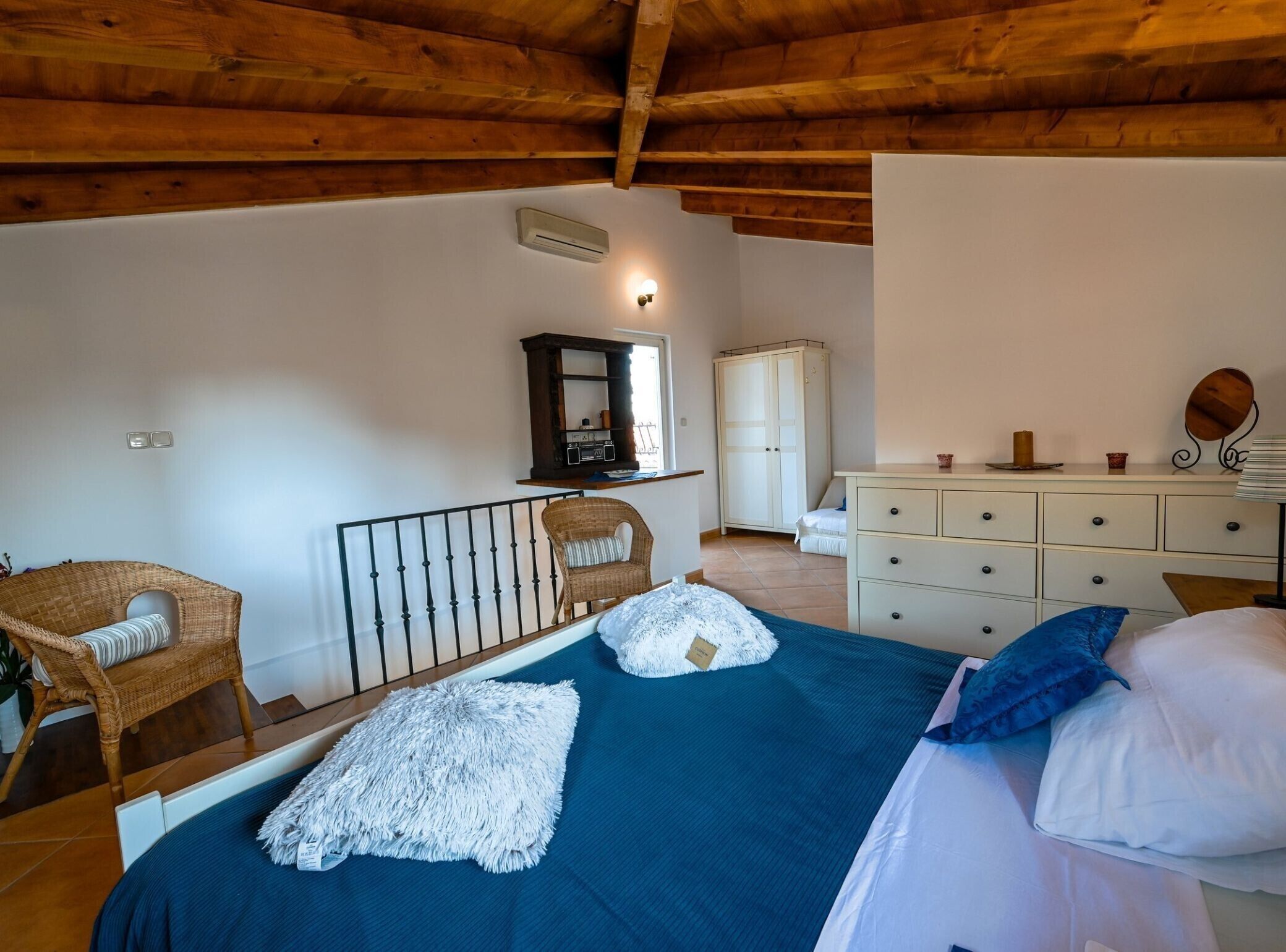 A bedroom with a bed, two chairs, a dresser, a wardrobe, and a mirror.