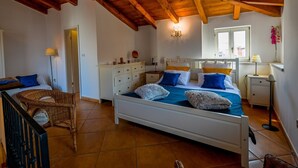 Een slaapkamer met een houten plafond, een bed met blauw beddengoed, een nachtkastje, een stoel en een raam met uitzicht.