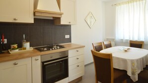 Une cuisine moderne équipée d’une cuisinière à gaz, d’un four et de meubles blancs. On y trouve une table à manger avec des chaises et une fenêtre avec des rideaux.