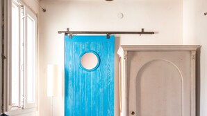 Ein Zimmer mit einer blauen Tür, einer weißen Tür und einem Fenster mit Vorhang.