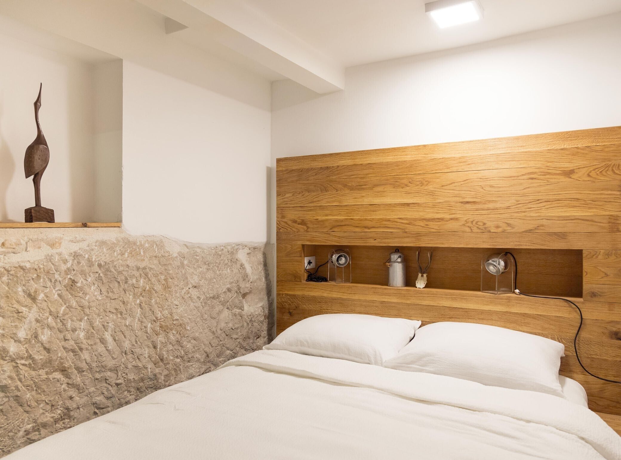 A bedroom with a stone headboard, wooden headboard, and a bed with white bedding.