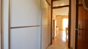 A hallway with a sliding door, a wooden door, and a tiled floor leading to a room with a bed and a window. - Coastal Breeze Apartment in Rovinj (Rovinj)