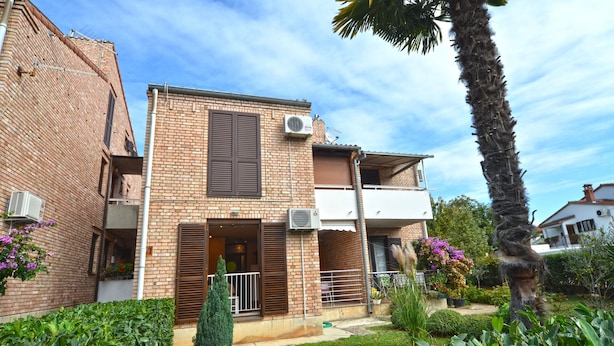 A two-story brick house with a balcony, air conditioning units, and a well-maintained garden with various plants and flowers. - Coastal Breeze Apartment in Rovinj (Rovinj)